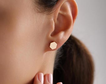 Può includere: Un paio di orecchini a bottone esagonali in oro. Gli orecchini sono piccoli e semplici e sarebbero un ottimo accessorio per tutti i giorni.