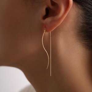 May include: A pair of gold earrings with a long, thin chain hanging from each. One earring has a curved, wavy design, while the other is a straight line.