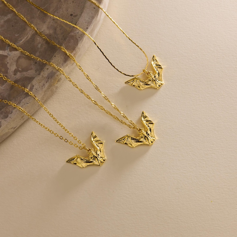 Puede incluir: Varios collares con colgantes de murci&eacute;lago dorados. Cada collar presenta un dije de murci&eacute;lago detallado suspendido de una delicada cadena. Los murci&eacute;lagos miran en diferentes direcciones, creando una exhibici&oacute;n din&aacute;mica. El fondo es de un beige claro neutro.