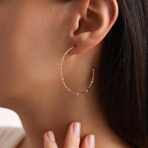 Può includere: Orecchini a cerchio dorati con piccole perle rotonde distanziate uniformemente attorno al cerchio.