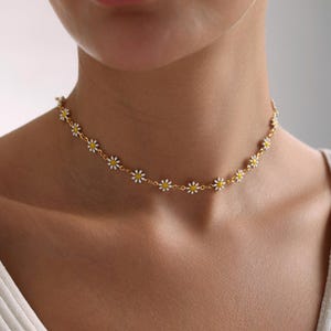 May include: A gold chain necklace with small white and yellow daisy flowers. The necklace is delicate and dainty.