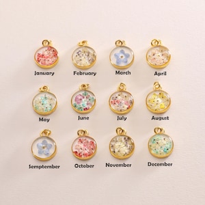 May include: Twelve gold pendants, each with a month's name and a floral arrangement encased in clear resin. The months are labelled January to December, with a variety of colourful flowers. Each pendant is circular.