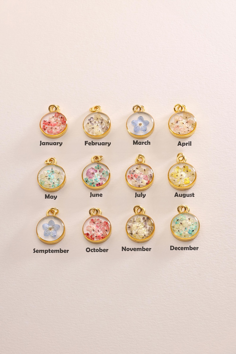 May include: Twelve gold pendants, each with a month's name and a floral arrangement encased in clear resin. The months are labelled January to December, with a variety of colourful flowers. Each pendant is circular.