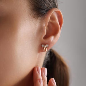 May include: Gold bow-shaped earrings with small clear stones.