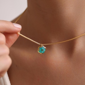 May include: A gold chain necklace with a hexagonal pendant featuring a pressed blue flower.