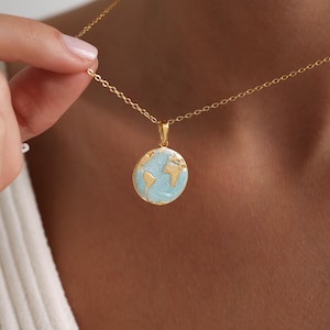 Puede incluir: Un collar de cadena dorada con un pequeño colgante redondo que presenta un diseño de globo terráqueo azul y dorado.