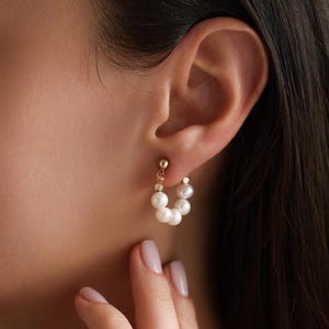 May include: Gold hoop earrings with a row of white pearls. The earrings are worn in a person's ear.