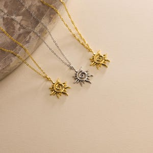 May include: Three necklaces with sun pendants. Two are gold-toned, and one is silver-toned. Each pendant features a spiral center with radiating rays. The chains are delicate and hang at varying lengths, creating a layered effect.