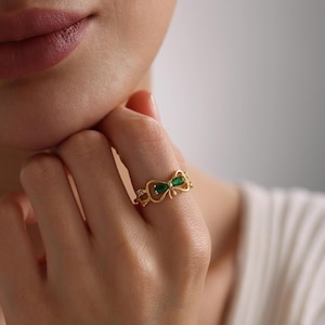 May include: A gold ring with a green bow design. The bow is made of two emerald-shaped stones.