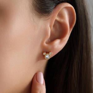 以下が含まれることがあります： 中央に小さな透明なクリスタル、両側にさらに小さなクリスタルが2つあり、ミッキーマウスの形をしたゴールドのスタッドピアスです。