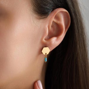 May include: Gold hexagon earrings with a dangling turquoise blue bead.