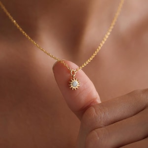 Pode incluir: Um delicado colar de corrente de ouro com um pequeno pingente de sol com uma pedra de opala branca.