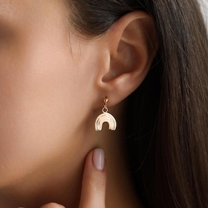 May include: Gold rainbow earrings with a textured finish. The earrings are small and delicate, and they would make a great gift for a friend or loved one.