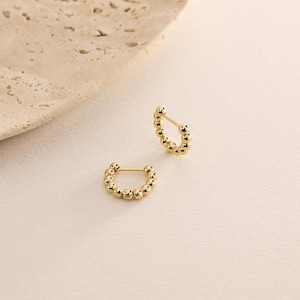 May include: A pair of gold hoop earrings with a beaded design. The earrings are small and delicate.