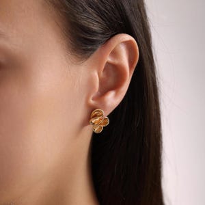 Puede incluir: Pendientes de color dorado con un diseño floral. Los pendientes son pequeños y delicados, y son perfectos para el uso diario.