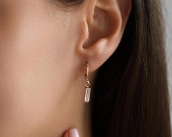 Puede incluir: Aretes de aro de oro con una piedra rectangular transparente colgante.