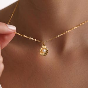 May include: A gold chain necklace with a seashell pendant. The seashell is open and contains a small pearl.