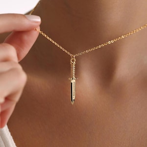 May include: A gold chain necklace with a dagger pendant. The dagger is detailed with a textured surface.