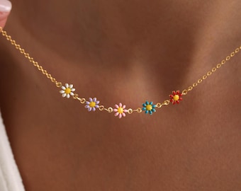 May include: A delicate gold chain necklace featuring five colorful daisy flower pendants. The daisy pendants are white, purple, pink, blue, and red with yellow centers. The necklace is a stylish accessory.