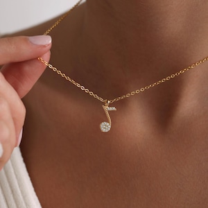 Op de afbeelding: Een gouden ketting met een klein, glinsterend muzieknoot-hanger. De hanger is gemaakt van goud en heeft kleine, heldere stenen die in de vorm van een muzieknoot zijn gezet.