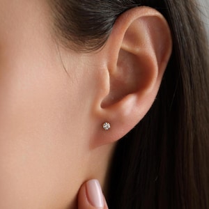 May include: A close-up of a person's ear with a small, clear diamond stud earring.