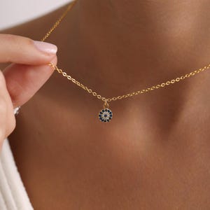 Könnte beinhalten: Eine goldene Kettenkette mit einem kleinen, runden Anhänger, der ein blaues böses Auge mit weißen Akzenten zeigt.