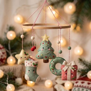 May include: A hanging mobile featuring felt ornaments suspended from a wooden hoop by red and white twine. The ornaments include a yellow star, a green Christmas tree, a green stocking, a green wreath, and a red gift box with a bow.