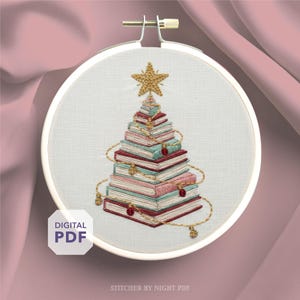 May include: Embroidered Christmas tree design in a white hoop. The tree is made of stacked books in shades of red, pink, and teal, topped with a gold star. Gold thread accents and a "DIGITAL PDF" label are visible.