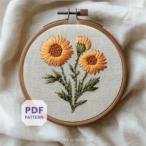 May include: An embroidered floral design featuring three orange flowers with green leaves, set within a wooden embroidery hoop. The text "PDF PATTERN" is visible. The design is on a light-colored fabric.