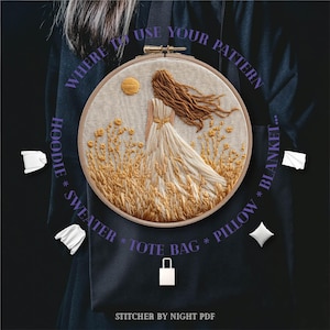 May include: An embroidered hoop art piece featuring a woman in a flowing dress standing in a field of wheat. The artwork is in shades of beige, brown, and gold. Text includes "WHERE TO USE YOUR PATTERN" and "HOODIE * SWEATER * TOTE BAG * PILLOW * BLANKET..."