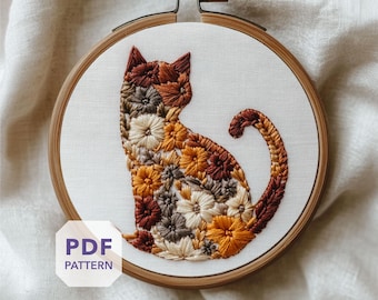 May include: An embroidery hoop featuring a cat silhouette filled with floral embroidery in shades of brown, orange, and cream. The wooden hoop holds the design on white fabric. The text "PDF PATTERN" is visible.
