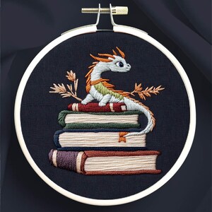 K&ouml;nnte beinhalten: Handgesticktes Design in einem runden Rahmen mit einem Drachen auf einem B&uuml;cherstapel. Der Drache ist wei&szlig;, orange und gr&uuml;n. Die B&uuml;cher sind verschiedenfarbig. Der Text oben lautet "DRAGON & BOOKS". Der Text unten lautet "modern hand embroidery pdf patterns".