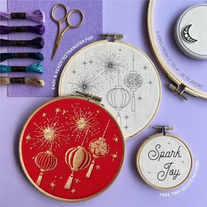 Puede incluir: Una variedad de bastidores de bordado con dise&ntilde;os de linternas, incluyendo un bastidor rojo con hilo dorado y otro blanco con contorno negro. La imagen tambi&eacute;n muestra hilo de bordar, tijeras y el texto "Spark Joy".