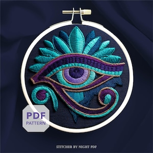 Puede incluir: Obra de arte bordada con el Ojo de Horus en tonos turquesa, morado y dorado, sobre una tela azul oscuro. El diseño está enmarcado en un bastidor de bordado blanco. El texto "PDF PATTERN" es visible. El texto "STITCHER BY NIGHT PDF" también es visible.