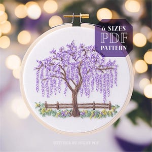 Op de afbeelding: Een borduurpatroon van een paarse wisteria-boom in een houten borduurring. Het patroon bevat een hek en groen gebladerte. De tekst "6 SIZES PDF PATTERN" wordt boven de ring weergegeven.
