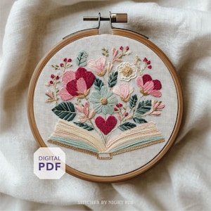 Könnte beinhalten: Gesticktes Blumendesign in einem Holzreifen. Das Kunstwerk zeigt einen Strauß aus rosa, roten und blauen Blumen, ein rotes Herz und ein offenes Buch. Die Worte "DIGITAL PDF" stehen in einem weißen Feld unten links.