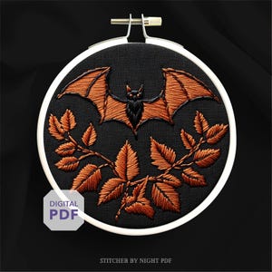 May include: Embroidered bat and leaf design in a white hoop on black fabric. The bat has orange wings and a black body. The leaves are orange. The words "DIGITAL PDF" are on a white tag. The text "STITCHER BY NIGHT PDF" is at the bottom.