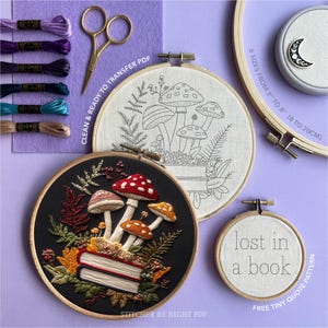 May include: An array of embroidery items, including finished hoops and supplies. Features a black hoop with a mushroom and book design, a white hoop with a mushroom outline, and a small hoop with the text "lost in a book". Also shown are embroidery floss, scissors, and a moon pin.