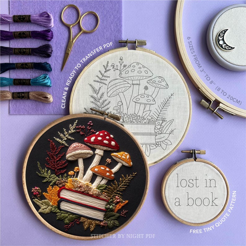 May include: An array of embroidery items, including finished hoops and supplies. Features a black hoop with a mushroom and book design, a white hoop with a mushroom outline, and a small hoop with the text "lost in a book". Also shown are embroidery floss, scissors, and a moon pin.