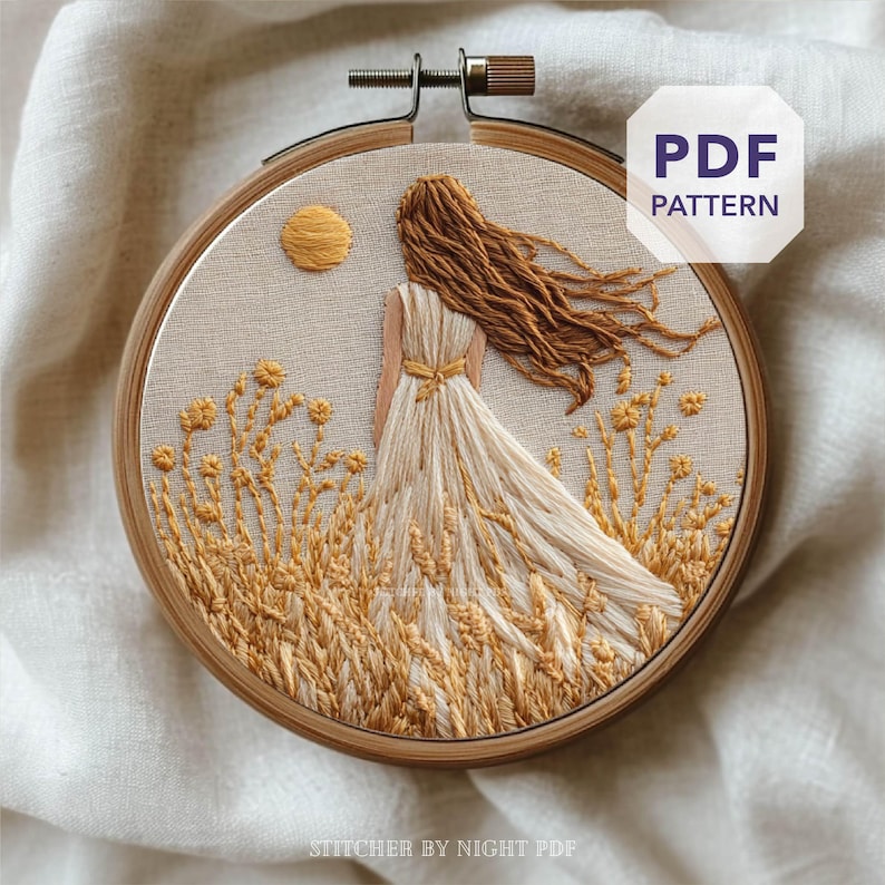 May include: Embroidered hoop art featuring a woman in a flowing white dress standing in a wheat field, with a yellow sun in the background. The embroidery is in shades of yellow and brown, with the text "PDF PATTERN" visible.