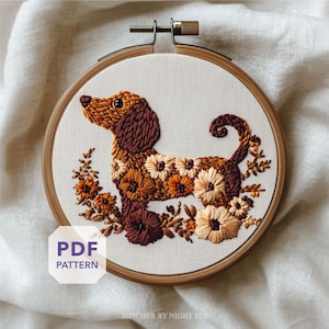Puede incluir: Un bordado de un perro salchicha en un aro de madera. El perro es marrón y beige, con detalles florales en tonos naranja, crema y marrón. El texto "PDF PATTERN" está en un recuadro blanco.
