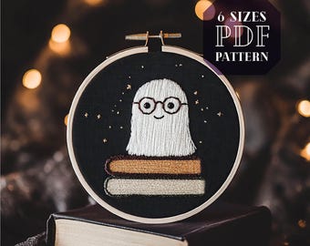 Op de afbeelding: Een zwarte borduurring met een witte geest die een bril draagt en op een stapel boeken zit. De achtergrond is donkerblauw met gouden sterren. De tekst "6 SIZES PDF PATTERN" staat in een witte doos met een zwarte rand.