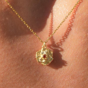 May include: A gold chain necklace with a delicate flower pendant featuring a red gemstone in the center.