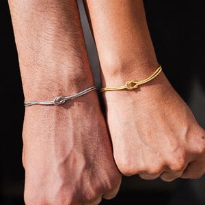 May include: Two matching bracelets with a knot design. One bracelet is silver and the other is gold.