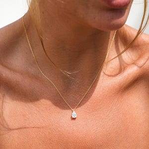 May include: A gold chain necklace with a teardrop-shaped pendant featuring a clear gemstone.