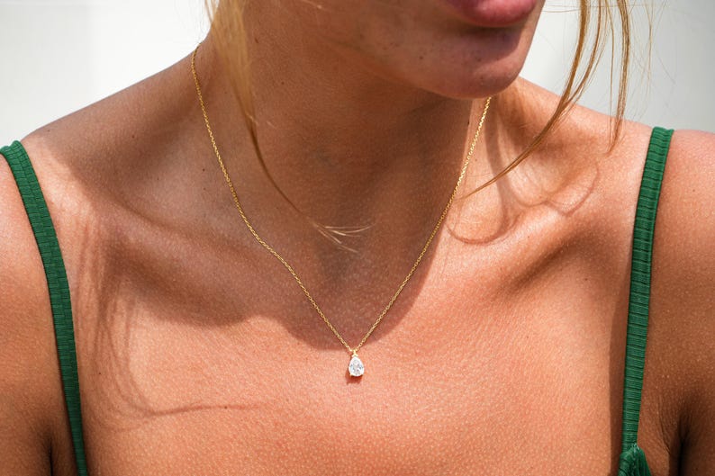May include: A gold chain necklace with a teardrop-shaped pendant featuring a clear gemstone.