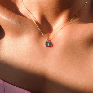 May include: A delicate gold chain necklace with a teardrop-shaped blue gemstone pendant.