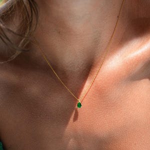 May include: A gold chain necklace with a small, teardrop-shaped green gemstone pendant.