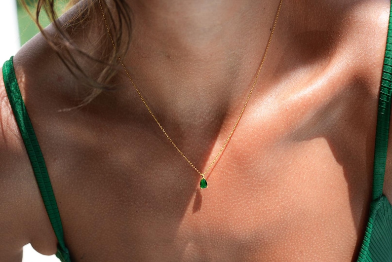 May include: A gold chain necklace with a small, teardrop-shaped green gemstone pendant.