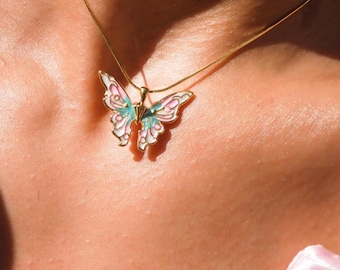 Può includere: Una collana con catena dorata con un ciondolo a forma di farfalla rosa e blu. La farfalla ha un centro bianco e un contorno dorato.